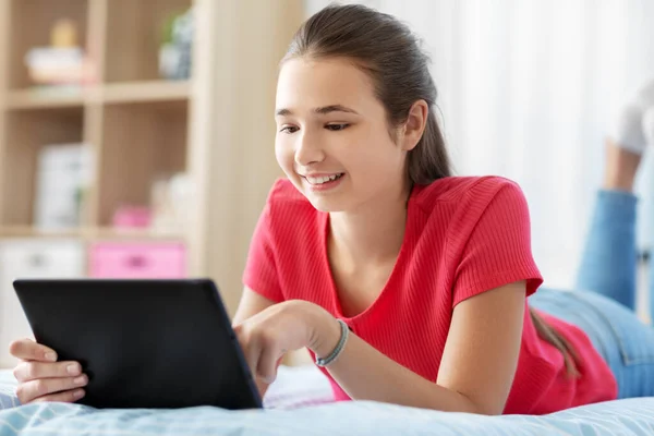 Chica sonriente con tableta PC acostado en la cama en casa —  Fotos de Stock