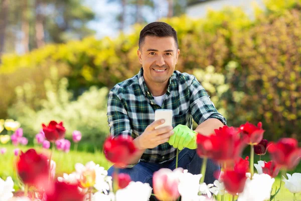 Hombre de mediana edad con teléfono inteligente en el jardín de flores —  Fotos de Stock