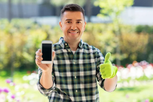 Homem com smartphone mostrando polegares no jardim — Fotografia de Stock
