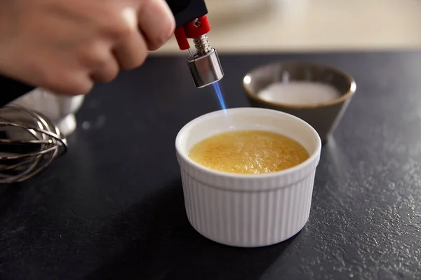 Рука с горелкой делает сахарную корочку в выпечке блюдо — стоковое фото