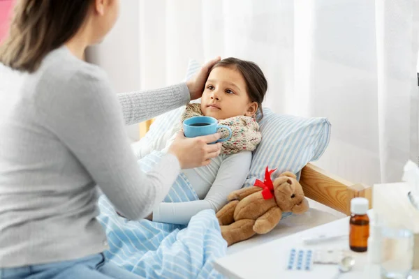 Madre dando té caliente a la pequeña hija enferma —  Fotos de Stock