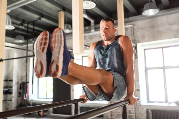 Hombre flexionar abdominales en barras paralelas en el gimnasio — Foto de Stock