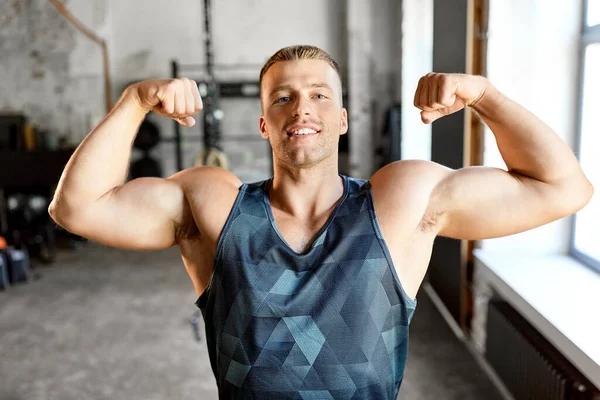 Šťastný mladý muž ukazuje své biceps svaly v tělocvičně — Stock fotografie