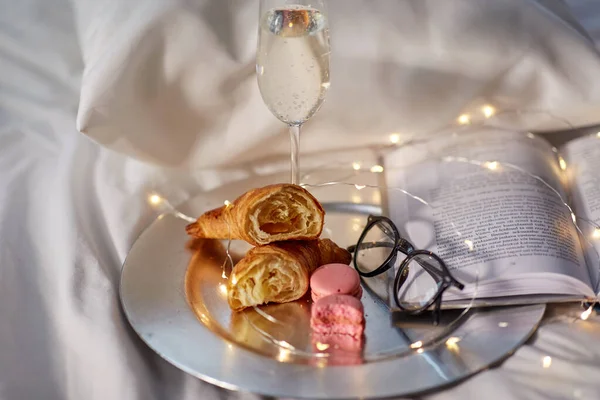 香槟、羊角面包、书籍和眼镜在床上 — 图库照片