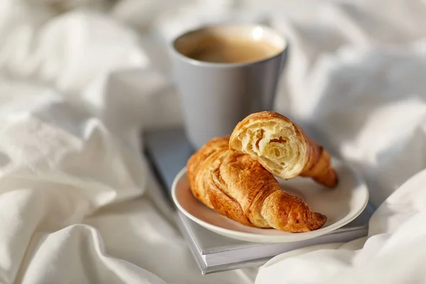 Croissants, tasse de café et réserver au lit à la maison — Photo