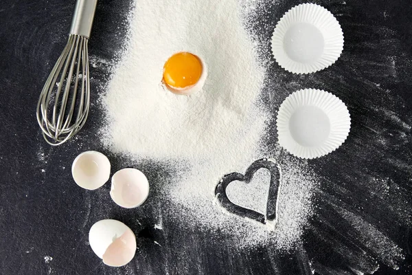Mehl, Ei, Schneebesen und Papierbackformen auf dem Tisch — Stockfoto