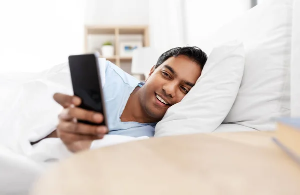 Hombre indio feliz con teléfono inteligente en la cama en casa — Foto de Stock