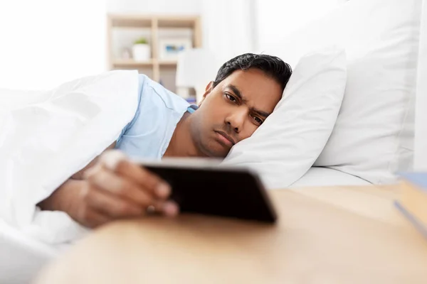 Hombre indio soñoliento con teléfono inteligente acostado en la cama — Foto de Stock