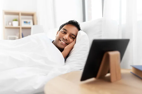Indiaanse man op zoek naar tablet pc in bed thuis Stockafbeelding