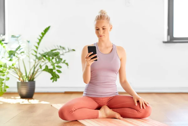 Женщина со смартфоном дома или в студии йоги — стоковое фото