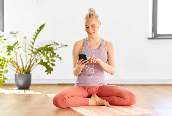 Donna con telefono e auricolari che fa yoga a casa — Foto Stock