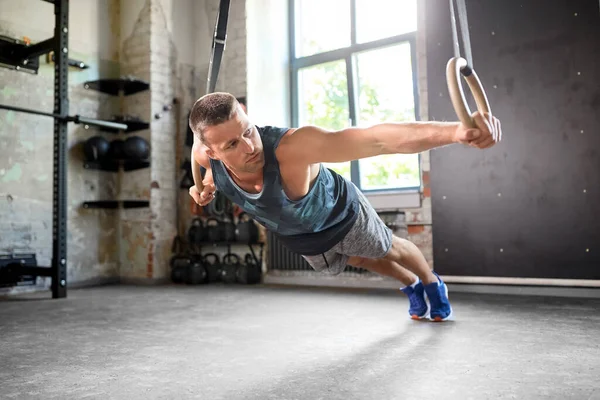 Hombre haciendo ejercicio en anillos de gimnasia en el gimnasio — Foto de Stock