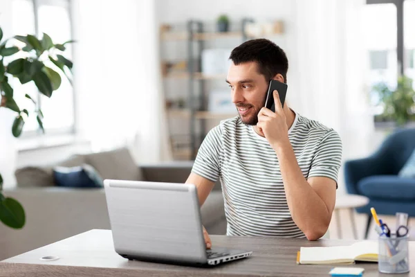 Hombre con el ordenador portátil llamando por teléfono en la oficina en casa — Foto de Stock