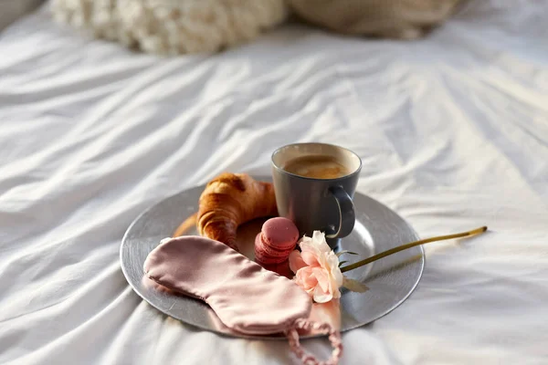 Croissant, kávé és szem alvás maszk az ágyban — Stock Fotó