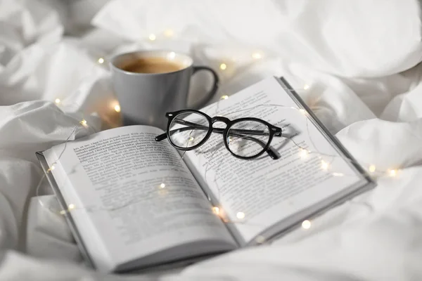 床上的咖啡、书、眼镜和花环 免版税图库图片