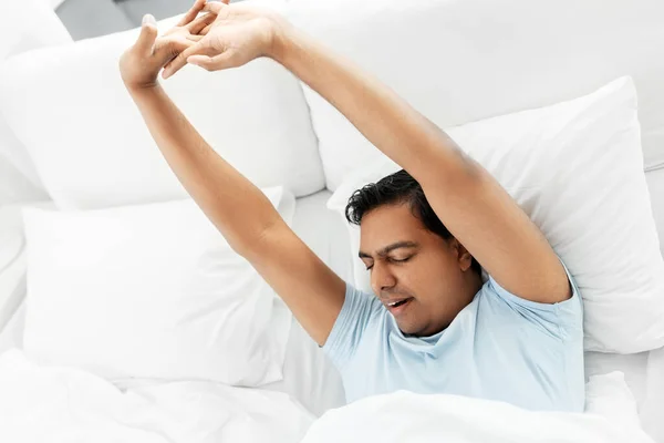 Hombre indio soñoliento estirándose en la cama en casa —  Fotos de Stock