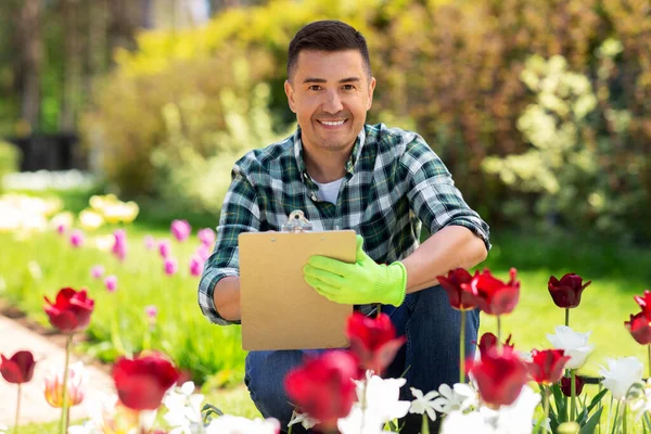 Mężczyzna ze schowkiem i kwiatami w ogrodzie letnim — Zdjęcie stockowe