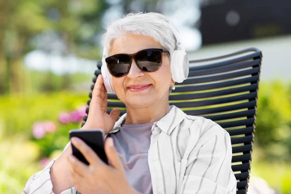 Mulher velha com fones de ouvido e smartphone no jardim — Fotografia de Stock