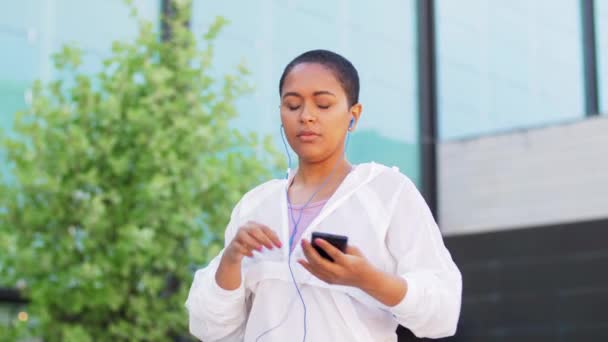 Woman with earphones and phone running outdoors — Stock Video