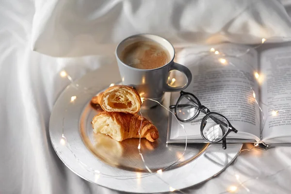 Croissants, Kaffee, Buch und Gläser im Bett — Stockfoto