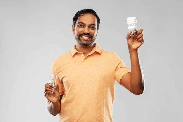 Smiling indian man comparing different light bulbs — Stock Photo, Image