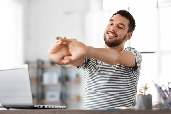 Homem feliz com laptop alongamento no escritório em casa — Fotografia de Stock