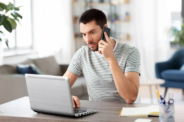 Hombre con el ordenador portátil llamando por teléfono en la oficina en casa — Foto de Stock