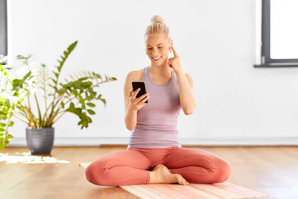 Donna con telefono e auricolari che fa yoga a casa — Foto Stock