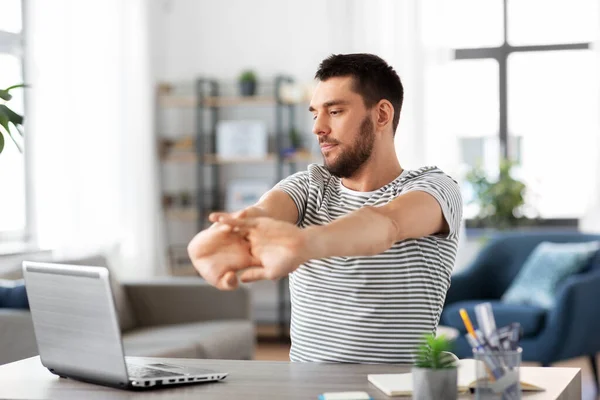 Man with laptop stretching at home office — Stock Photo, Image