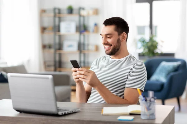 Hombre con teléfono inteligente y portátil en la oficina en casa — Foto de Stock