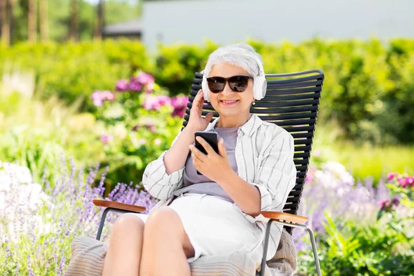 Стара жінка з навушниками та смартфоном в саду — стокове фото