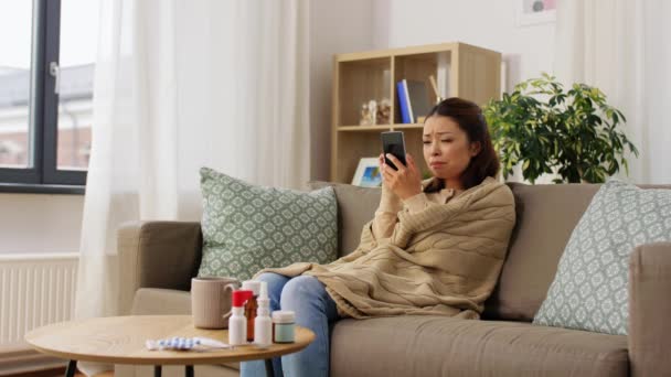 躺在毯子里的悲伤的女人在家里用智能手机 — 图库视频影像