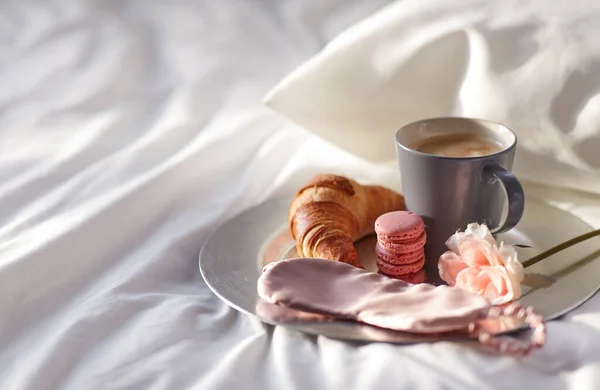 Croissant, koffie en oog slaapmasker in bed — Stockfoto