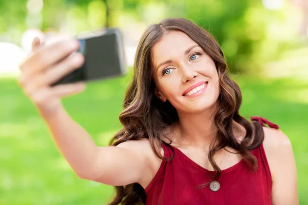 Счастливая женщина со смартфоном делает селфи в парке — стоковое фото