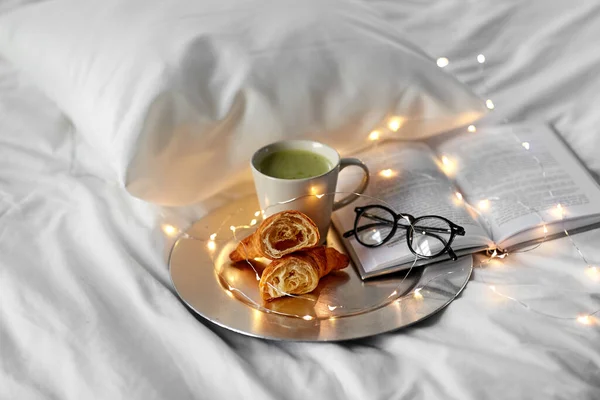 Croissants, Matcha-Tee, Buch und Gläser im Bett — Stockfoto