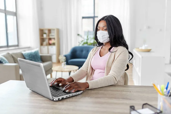 Mujer en la máscara con el ordenador portátil de trabajo en casa oficina — Foto de Stock