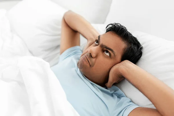 Annoyed indian man lying in bed and closing ears — Stock Photo, Image