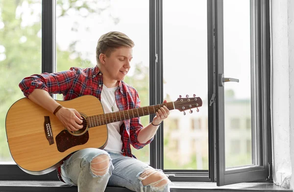 Young man playing guitar sitting on windowsill — Stock Photo, Image