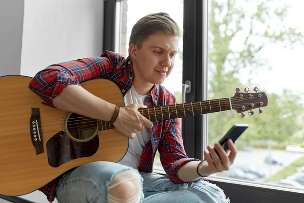 Giovane uomo che suona la chitarra seduto sul davanzale della finestra — Foto Stock