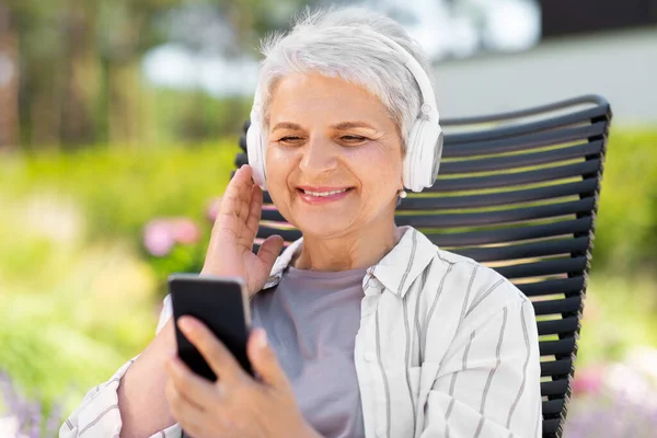 Idős nő fülhallgatóval és okostelefonnal a kertben — Stock Fotó
