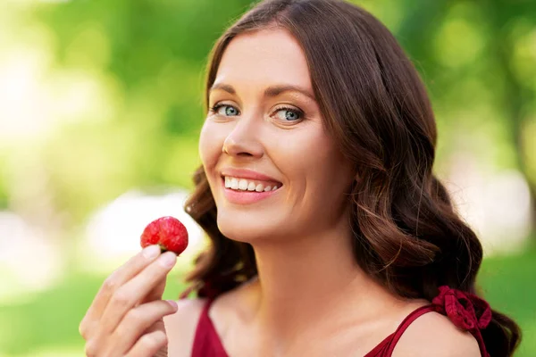 Glad kvinna äter jordgubbar i sommarparken — Stockfoto