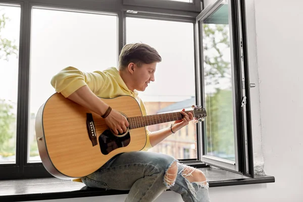Mladý muž hraje na kytaru sedící na parapetu — Stock fotografie