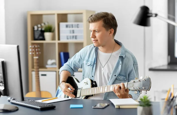 Joven con ordenador tocando la guitarra en casa —  Fotos de Stock