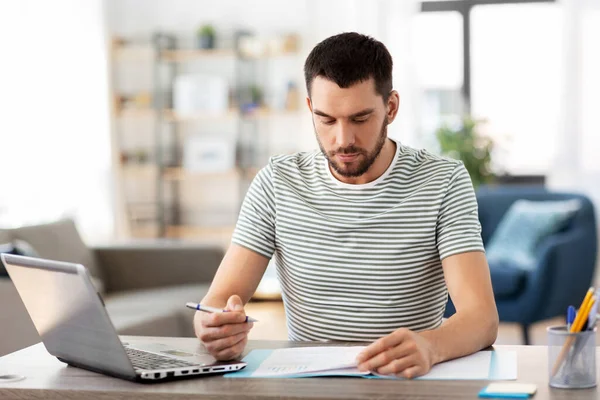 Homem com papéis e laptop trabalhando no escritório em casa — Fotografia de Stock