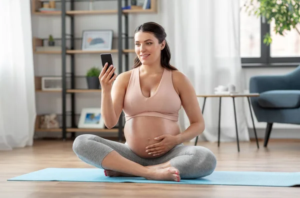 Mulher grávida feliz com telefone fazendo ioga em casa — Fotografia de Stock
