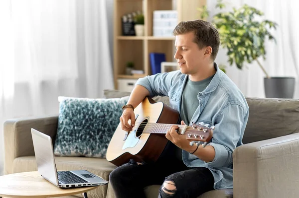 Joven con portátil tocando la guitarra en casa — Foto de Stock