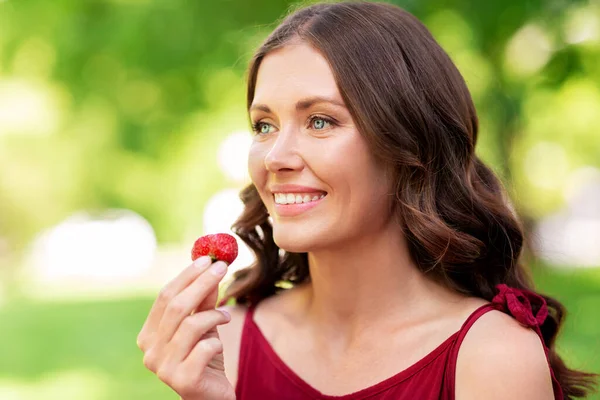 Happy woman eating strawberry at summer park — Stock Photo, Image