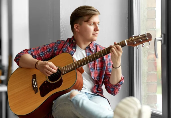 Молодой человек играет на гитаре, сидя на подоконнике — стоковое фото