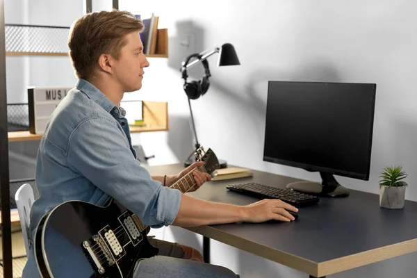 Молодой человек с компьютером и бас-гитарой дома — стоковое фото