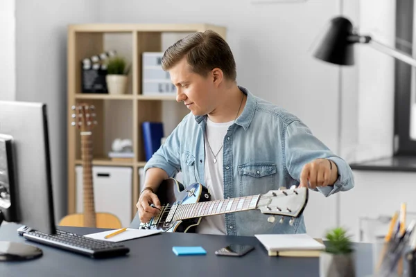 Joven con ordenador tocando la guitarra en casa — Foto de Stock